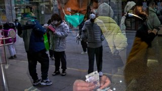 Visitors are reflected on a window pane as a man counts Chinese currency notes at a shop selling tea in Qianmen, a popular tourist spot in Beijing, Jan. 3, 2023.