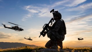Military Helicopters flying behind kneeling soldier at sunset