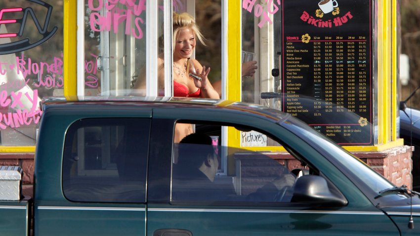 A barista at a Grab-N-Go Bikini Hut espresso stand holds money as she waves to a customer, Feb. 2, 2010, in Snohomish County, just outside the city limits of Everett, Wash.