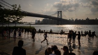 People gather at a water fountain in a park before the Manhattan skyline in the east river in New York on July 26, 2023.