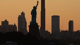 The sun rises behind the Statue of Liberty and the Brooklyn Tower on July 22, 2023, as seen from Jersey City, New Jersey.