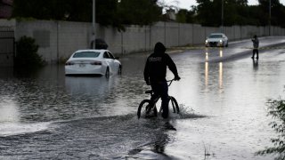 A cyclist rides through floodwaters near a stranded car, Friday, Sept. 1, 2023, in Las Vegas.