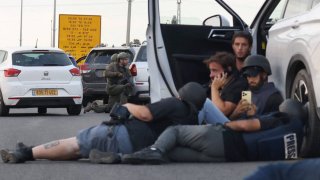 Journalists take cover behind cars as Israeli soldiers take position during clashes with Palestinian fighters near the Gevim Kibbutz, close to the border with Gaza on October 7, 2023.