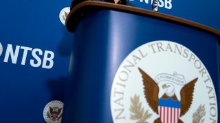 FILE – The National Transportation Safety Board logo and signage are seen at a news conference at NTSB headquarters in Washington, Dec. 18, 2017.