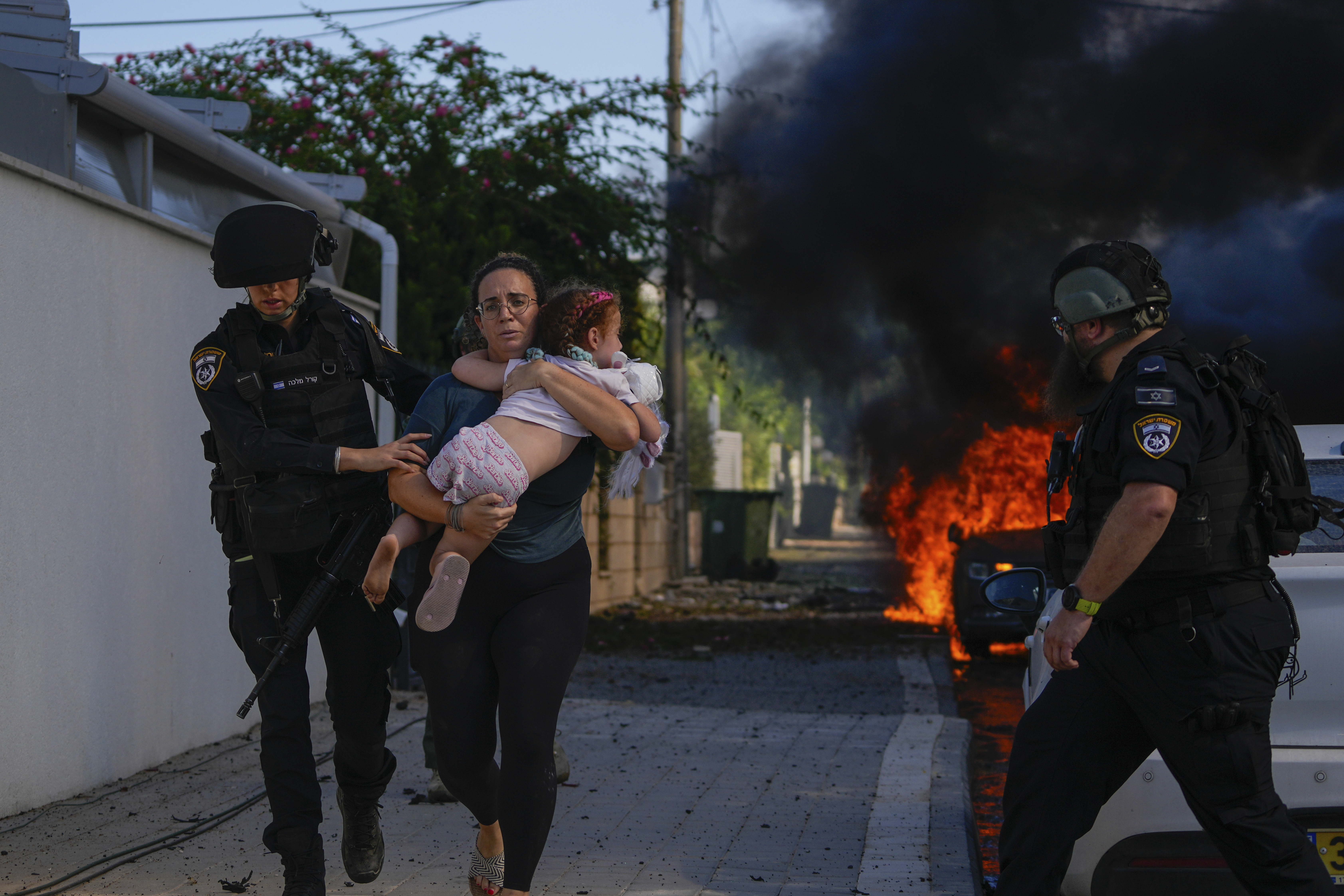 Police officers evacuate a woman and a child from a site hit by a rocket fired from the Gaza Strip in Ashkelon, southern Israel, Saturday, Oct. 7, 2023. The militant Hamas rulers of the Gaza Strip carried out an unprecedented, multi-front attack on Israel at daybreak Saturday, firing thousands of rockets as dozens of Hamas fighters infiltrated the heavily fortified border in several locations by air, land, and sea and catching the country off-guard on a major holiday.