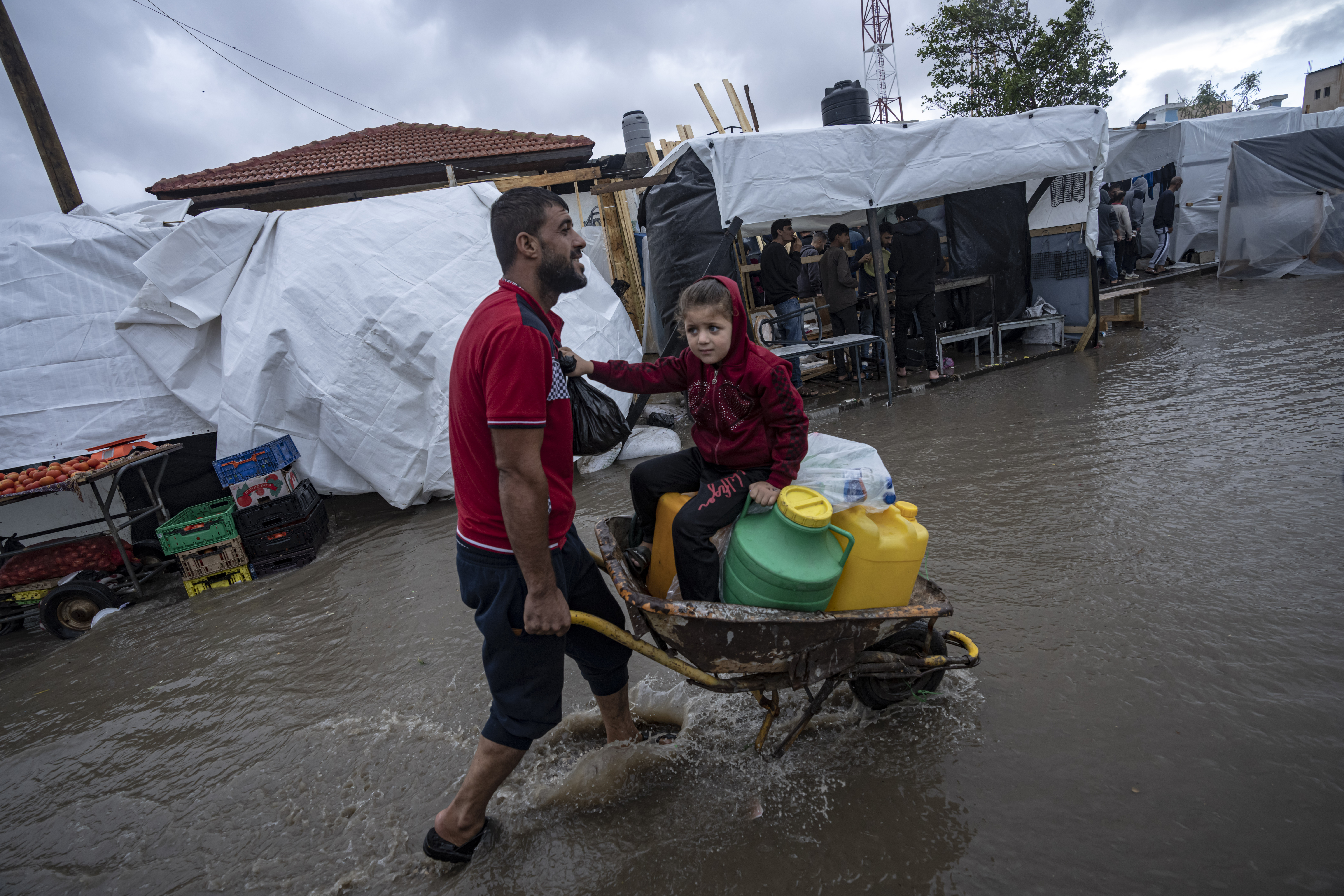 A man carries his daughter in a wheelbarrow through the flooded streets of a U.N. displacement camp after rainfall in the southern town of Khan Younis, Gaza Strip, Sunday, Nov. 19, 2023.