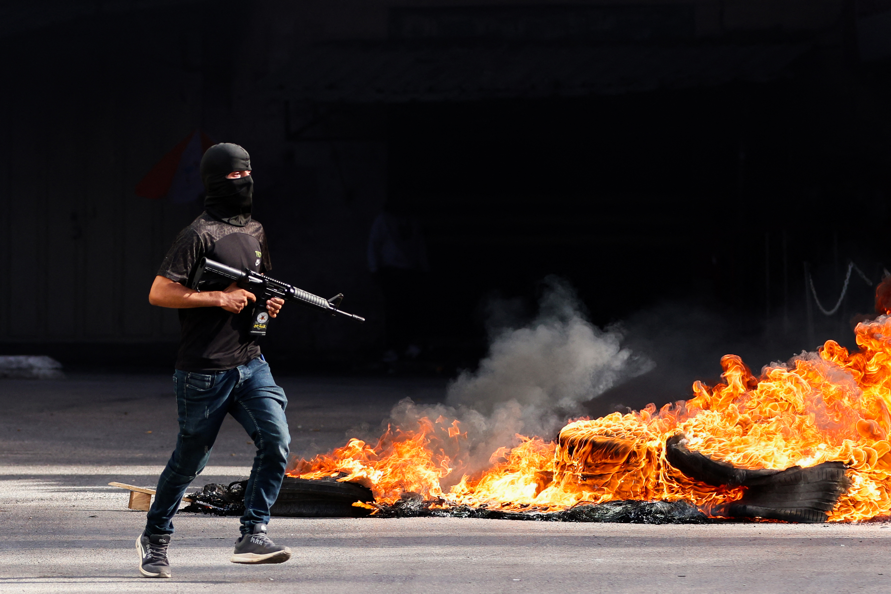 A Palestinian gunman runs past burning tires during confrontations with Israeli forces in the occupied West Bank city of Jenin on November 9, 2023.