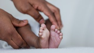 Mother holding her newborn baby sitting on a sofa bonding with her. They are at their home in Sedgefield, North East England. Focus is on the baby's feet as the mother touches them.