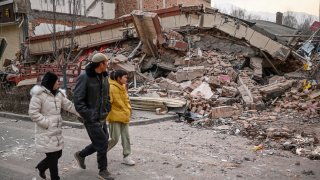 People walk past a collapsed building after an earthquake in Dahejia, Jishishan County in northwest China’s Gansu province on Dec. 19, 2023.