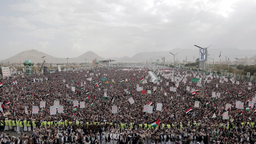 Yemenis lift rifles, flags of Yemen and Palestine, and Houthi emblems as they participate in a protest against Israel's continuing war in the Gaza Strip