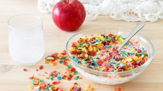 A bowl of fruity pebbles cereal with milk and a red apple.