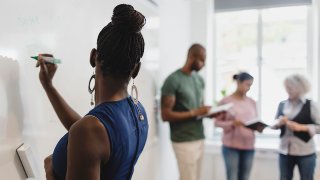 Woman holding pen looking at teacher and students standing in language class