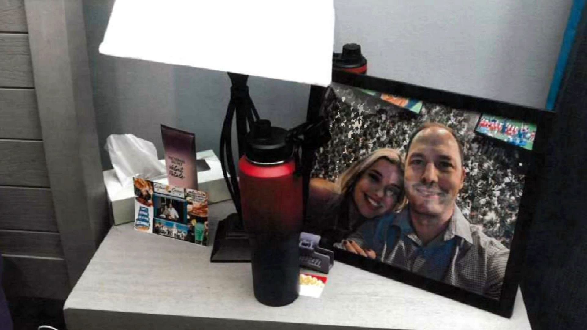 a nightstand with a lamp, pictures and a bottle