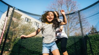 siblings have fun on trampoline under blue sky