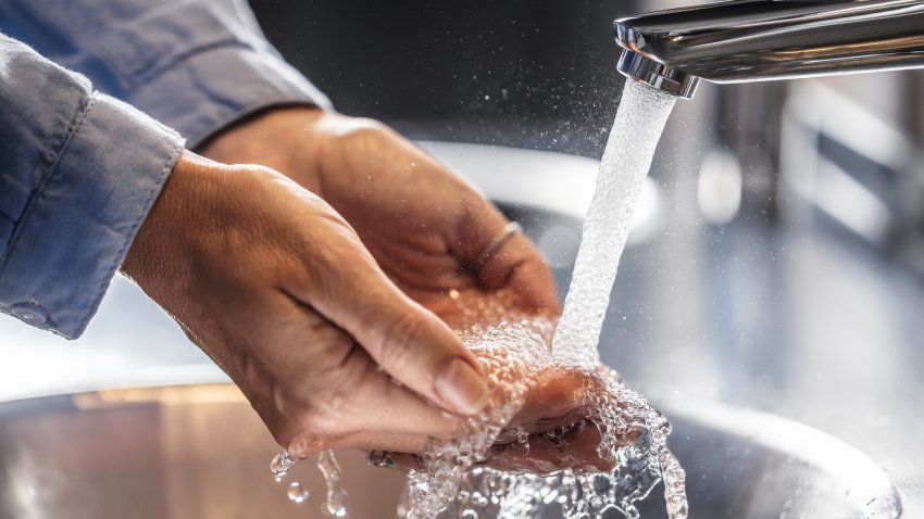 A view of a woman washing her hands under running water in a bathroom.