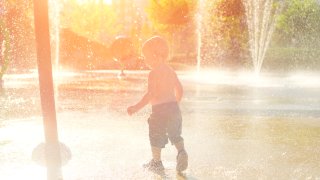 Happy child has fun playing in water fountains on hot day during summer. Boy playing in water at waterpark. A kid in spray park.