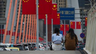 Two women sit on the sidewalk of Qiansimen Jialing River Bridge, decorated with Chinese national flags, on October 3, 2024 in Chongqing, China. National Day Golden Week is a holiday in China commemorates the founding of the People’s Republic of China in 1949. 