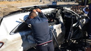 A man reacts in front of a car hit by an Israeli strike