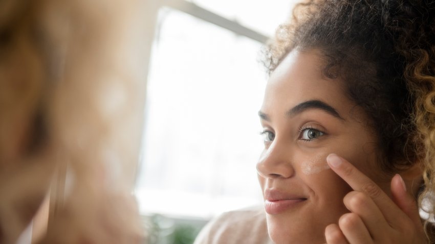 Mixed Race woman applying lotion to cheek