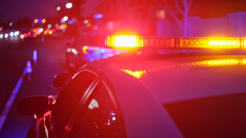 A police car at night alongside a road with emergency lights flashing.