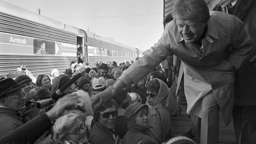 FILE - President-elect Jimmy Carter leans over to shake hands with some of the people riding the "Peanut Special" to Washington, Jan. 19, 1977. They will travel all night, arriving in Washington in time for Carter's inauguration as president on Jan. 20.