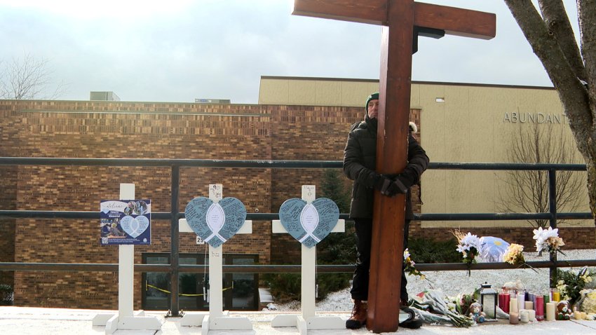 FILE – Dan Beazley stands with the homemade cross he brought from Michigan for victims of a shooting at Abundant Life Christian School Wednesday, Dec. 18, 2024, in Madison, Wis.