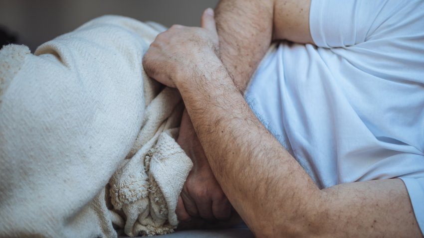 An unrecognizable man is suffering from abdominal pain lying on the bed crossed his arms in the stomach