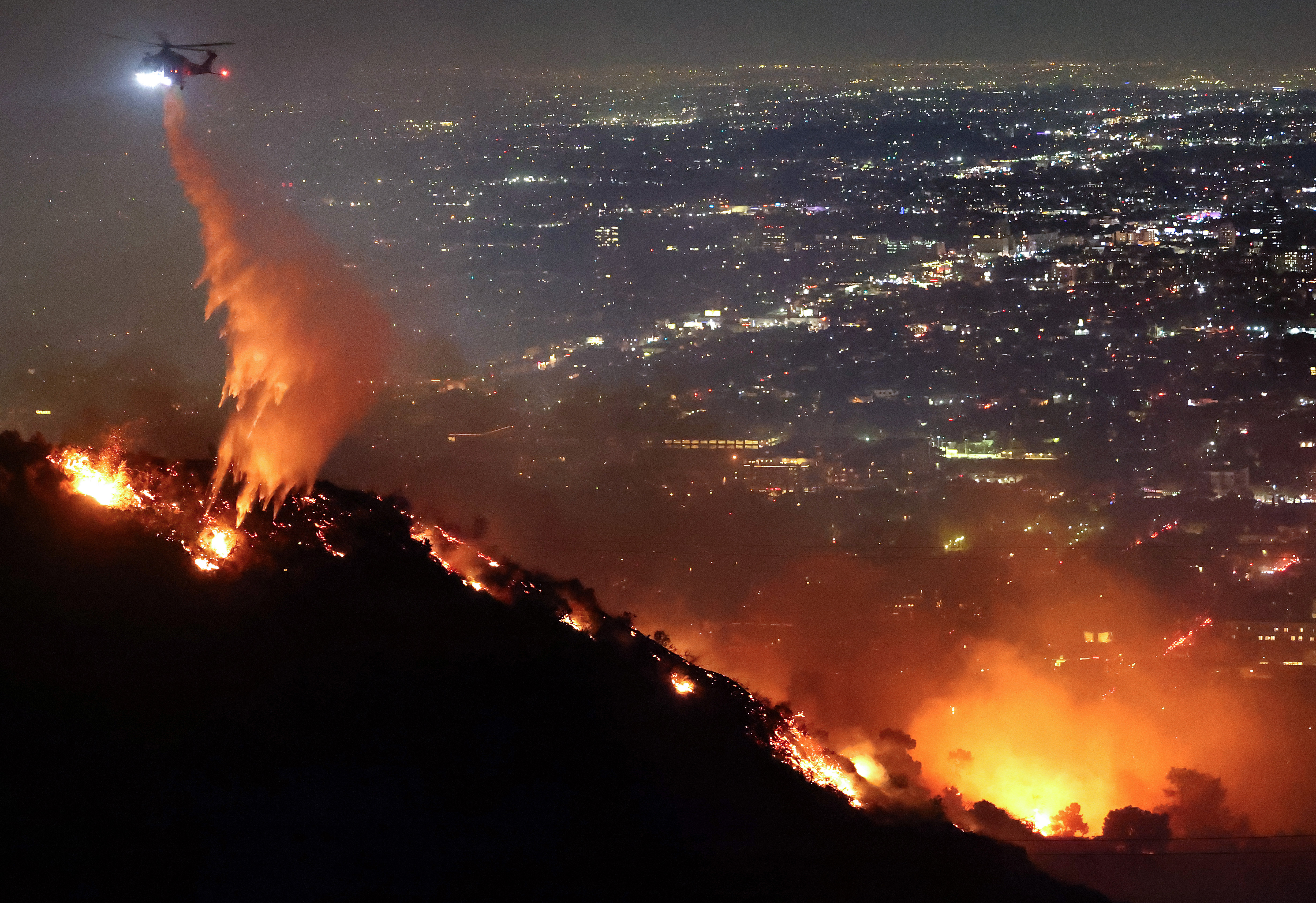 A firefighting helicopter drops water as the Sunset Fire burns in the Hollywood Hills on Jan. 8, 2025 in Los Angeles, California.