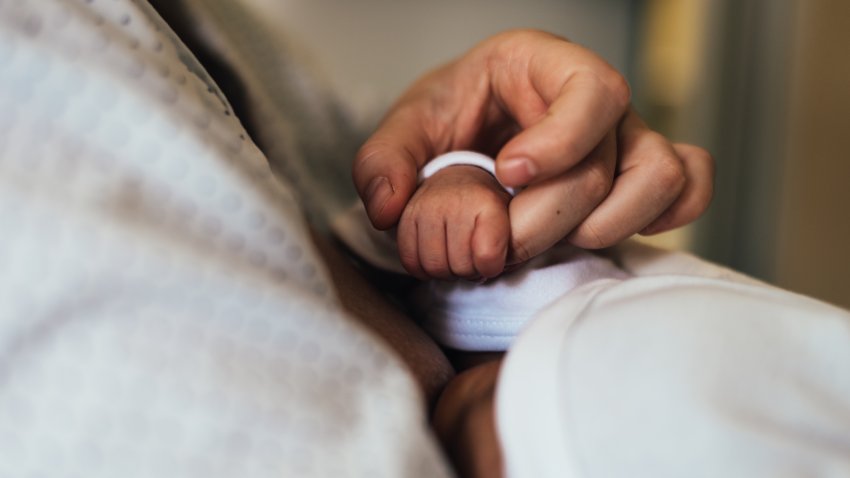 Mother’s hand holding her newborn baby’s hand while breastfeeding.