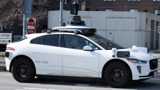 Waymo self-driving cars with roof-mounted sensor arrays traveling near palm trees and modern buildings along the Embarcadero, San Francisco, California, February 21, 2025.Β
