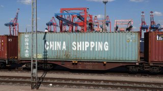 Shipping containers, including one of China Shipping, lie on flatbed railway cars as dock cranes stand behind at Hamburg Port on April 15, 2025 in Hamburg, Germany.