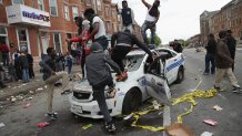 BALTIMORE, MD - APRIL 27: Demonstrators climb on a destroyed Baltimore Police car in the street near the corner of Pennsylvania and North avenues during violent protests following the funeral of Freddie Gray April 27, 2015 in Baltimore, Maryland. Gray, 25, who was arrested for possessing a switch blade knife April 12 outside the Gilmor Homes housing project on Baltimore's west side. According to his attorney, Gray died a week later in the hospital from a severe spinal cord injury he received while in police custody. (Photo by Chip Somodevilla/Getty Images)
