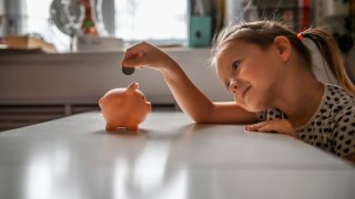 Girl Child Putting a Coin in a Piggy Bank.