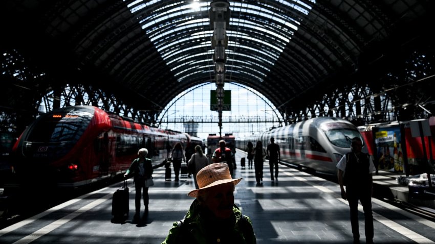 Passengers walk on a platform past ICE high speed train (R) and regional train at main railway station in Frankfurt am Main, western Germany, on May 20, 2025.