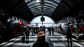 Passengers walk on a platform past ICE high speed train (R) and regional train at main railway station in Frankfurt am Main, western Germany, on May 20, 2025.