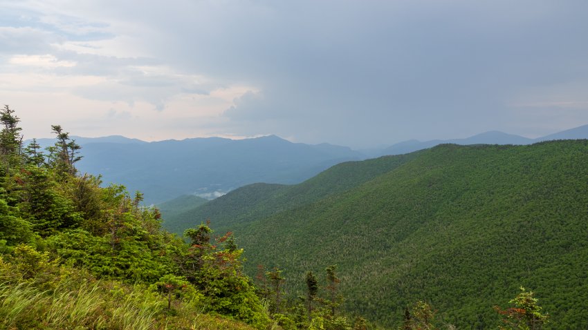 A view from Cascade Mountain’s summit, where rays of light pierce through heavy clouds, illuminating the Adirondacks in New York State.