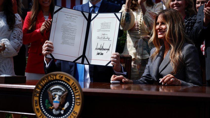 WASHINGTON, DC - MAY 19: U.S. President Donald Trump, seated next to first lady Melania Trump and joined by lawmakers and victims of AI deepfakes and revenge porn, holds a copy of the TAKE IT DOWN Act during a signing ceremony in the Rose Garden of the White House on May 19, 2025 in Washington, DC. The first lady made the Tools to Address Known Exploitation by Immobilizing Technological Deepfakes on Websites and Networks (TAKE IT DOWN) Act a priority, traveling to Capitol Hill to lobby lawmakers and show her support for the legislation, which addresses non-consensual intimate imagery, or "revenge porn," and artificial intelligence deepfakes posted online and to social media.