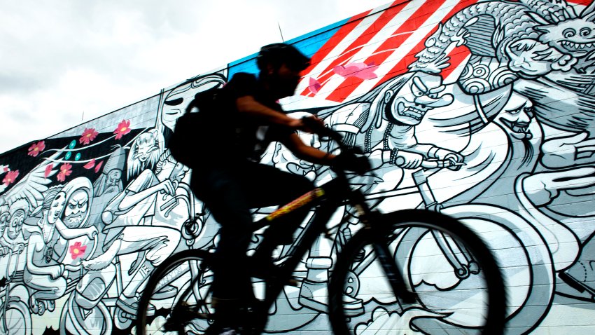 WASHINGTON, DC – MAY 13:  A cyclist zooms past a Cita Sadeli “Chelove” mural near 5th & T Street NE on the Metropolitan Branch Trail to downtown Washington, DC on May 13, 2015.    Friday, May 15th is DC’s Bike to Work Day.  The Commuter Connections and the Washington Area Bicyclist Association invite DC’s workforce to pedal to work and join several commuting convoys of experienced bicycle commuters to experience a fun and healthy way to get to the office.  They plan to have 79 pit stops along bike routes in the greater DC, VA, MD area that will offer refreshments, free t-shirts and a chance to win bicycles.  For more information go to biketoworkmetrodc.org.  (Photo by Linda Davidson / The Washington Post via Getty Images)