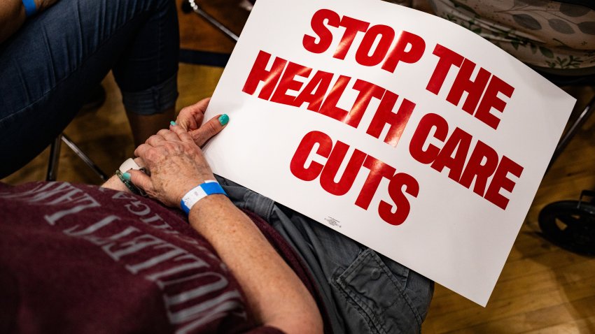 An attendee holds a “Stop The Health Care Cuts” sign during a town hall in Lansing, Michigan, US, on Friday, June 6, 2025. Republicans are betting they can win the semantic battle over the future of Medicaid, with a multi-trillion dollar tax bill at stake, while Democrats view the cuts as a welcome talking point to attack the president’s agenda. Photographer: Emily Elconin/Bloomberg via Getty Images