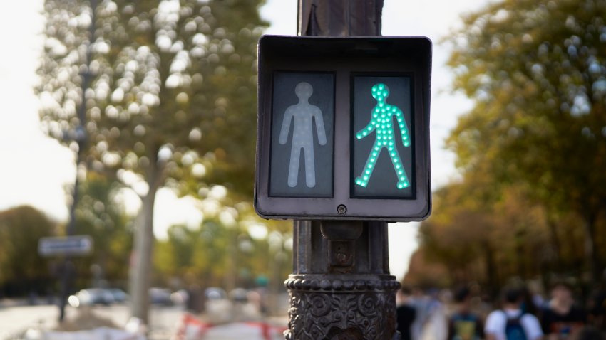close-up front view of a pedestrian traffic light with crossing signal in the streets of paris with people walking in the background